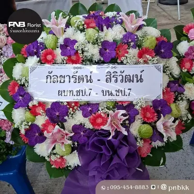 ภาพส่งจริง พวงหรีดดอกไม้สด โทนสีม่วง-ชมพู-ขาว จัดด้วยกล้วยไม้ม่วง ลิลลี่ชมพู เยอบีร่าชมพูแดง เบญจมาศขาว และลูกตีนเป็ดสีเขียว ประดับโบว์ผ้าม่วง ณ วัดศรีจันทร์ จ.ขอนแก่น ศาลาเตียฮั่วหยู